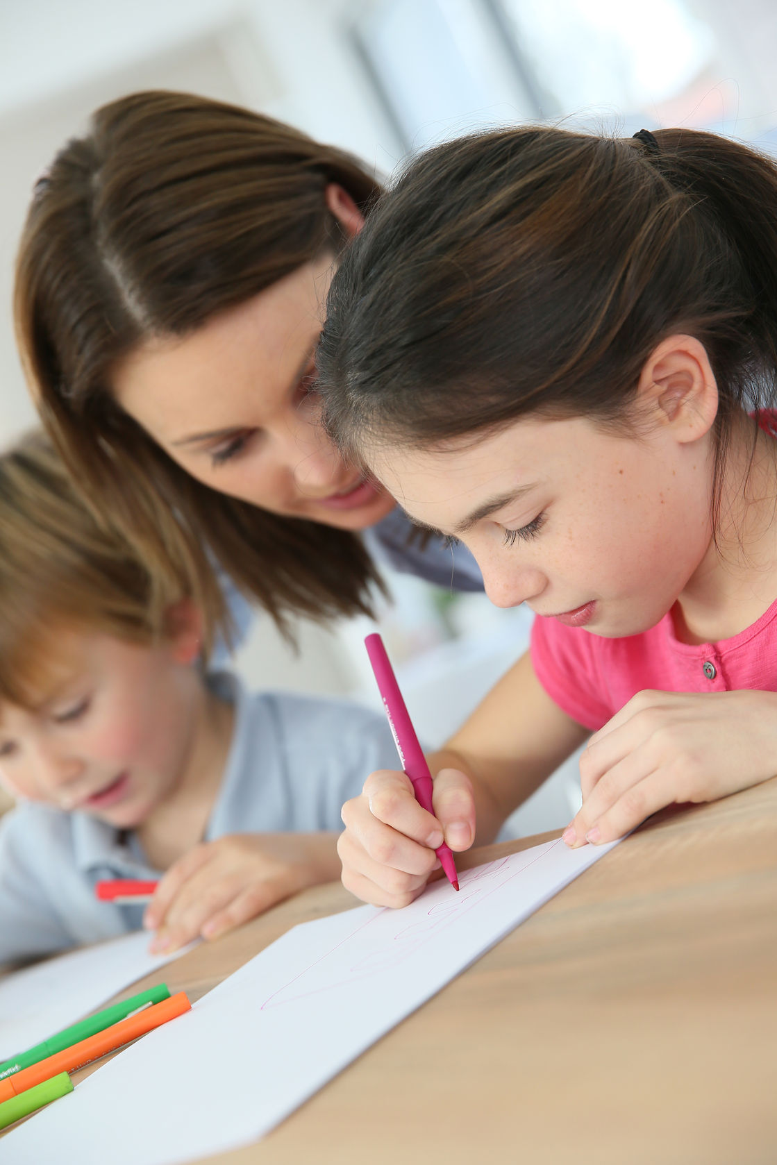 Kinder sitzen mit einem Erwachsenen am Tisch und lernen