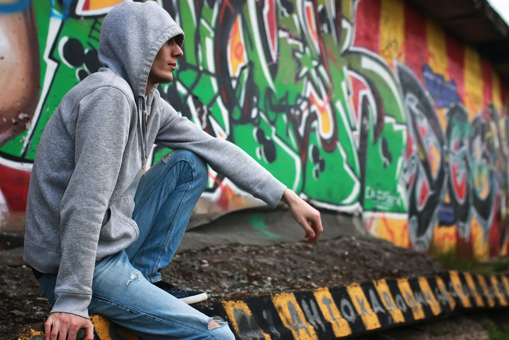 Mann sitzt im Kapuzenpullover vor einem Graffiti