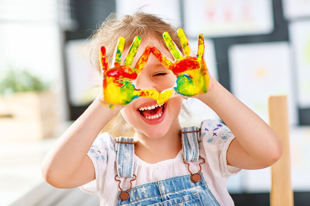 Kind mit bunt bemalten Händen freut sich