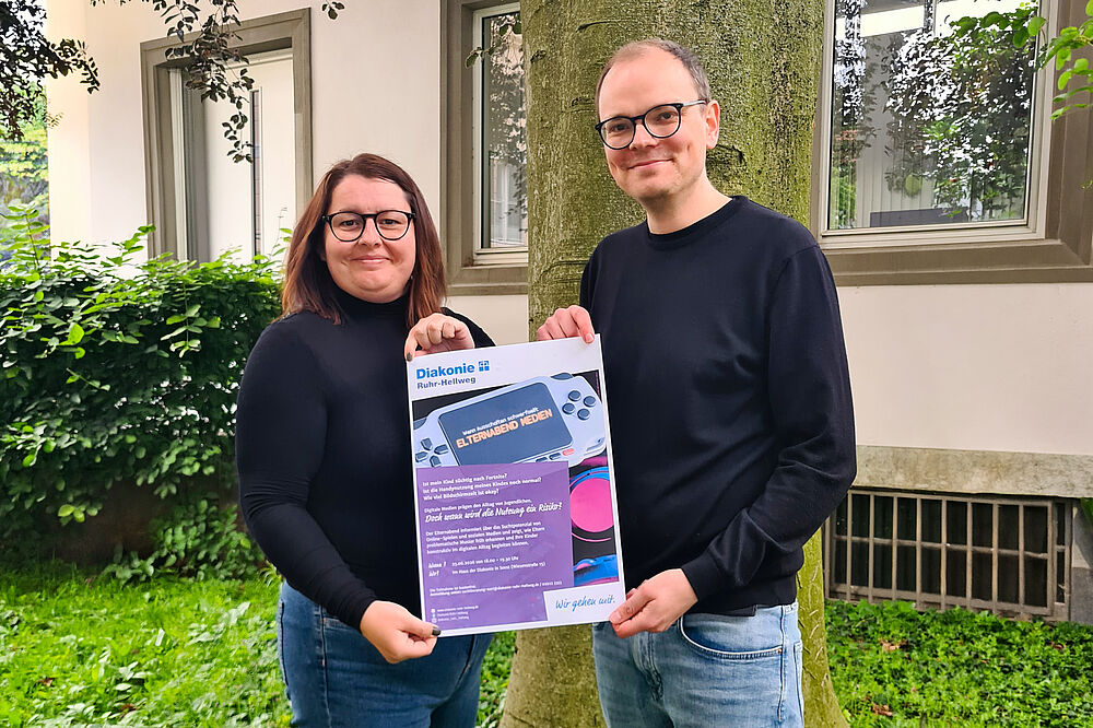 Zwei Mitarbeiter zeigen Plakat "Elternabend Medienkonsum"