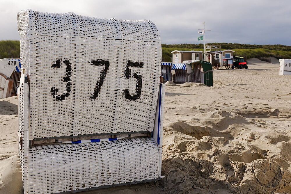 Das Bild zeigt einen Strandkorb im Sand vor Dünen