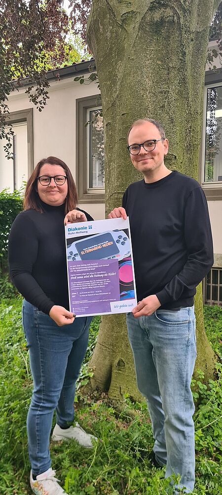 Zwei Mitarbeiter zeigen Plakat "Elternabend Medienkonsum"