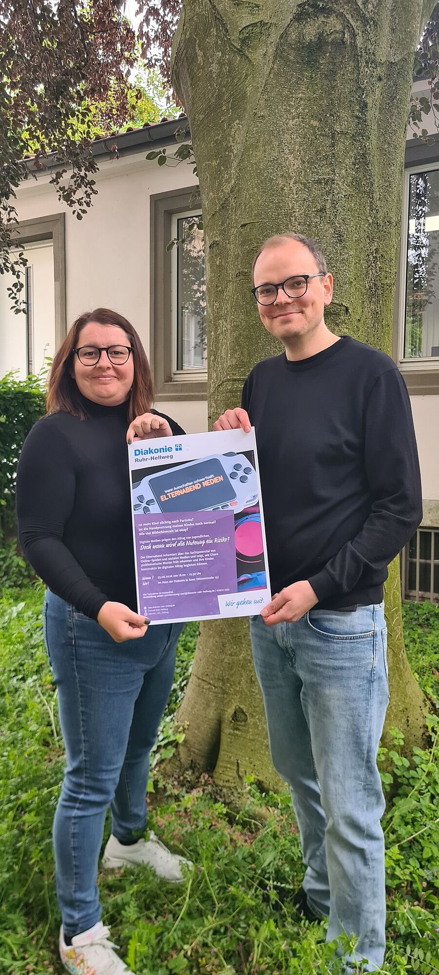 Zwei Mitarbeiter zeigen Plakat "Elternabend Medienkonsum"